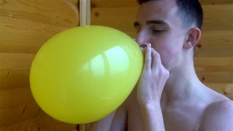 Young man trying to inflate a yellow balloon Stock Footage 82126695