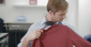 A young man trying on a red sweater in the store Stock Footage 86080151
