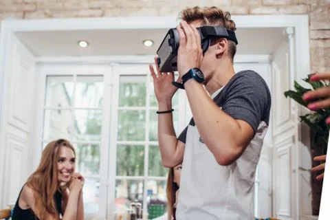 Young man trying virtual reality glasses while people looking at him and 스톡 사진