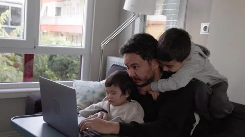 A young man trying to work at home with little son on hands and 6-years-old son Stock Footage 244828494