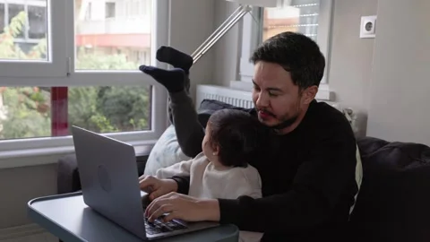A young man trying to work at home with little son on hands and 6-years-old son Stock Footage 244828660