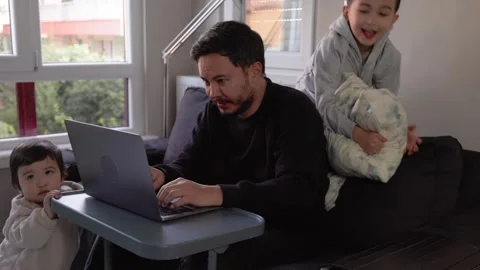 A young man trying to work at home with little son on hands and 6-years-old son Stock Footage 245424351
