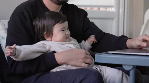 A young man trying to work on laptop holding his son at home. Remote work Stock Footage 244827378