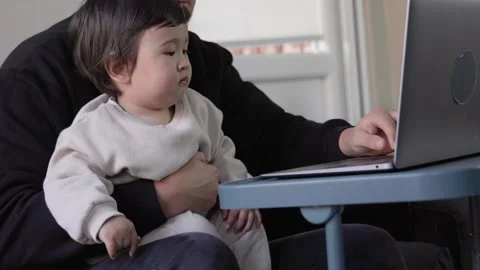 A young man trying to work on laptop holding his son at home. Remote work Stock Footage 244828480