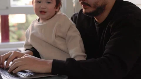 A young man trying to work on laptop holding his son at home. Remote work Stock Footage 244828509