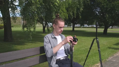 Young man tunes camera and takes picture sitting in garden Stock Footage 139797992