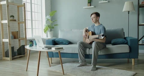A young man tunes a guitar using a laptop computer at home. Stock Footage 132102982