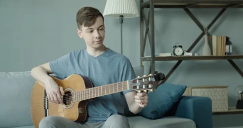 A young man tunes a guitar using a laptop computer at home. Stock Footage 132103175
