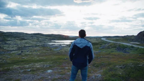 Young man turns his back and looks at the sunset near the summer hills in Norway Stock Footage 247345749