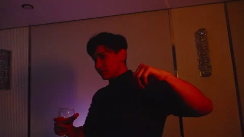 Young Man in Turtleneck Holding Wine Glass Dancing Under Neon Lighting Vidéo 345099688