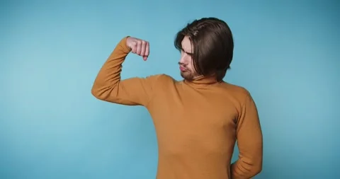 Young man in a turtleneck sweater flexes his bicep, showcasing confidence o.. Stock Footage 313280451