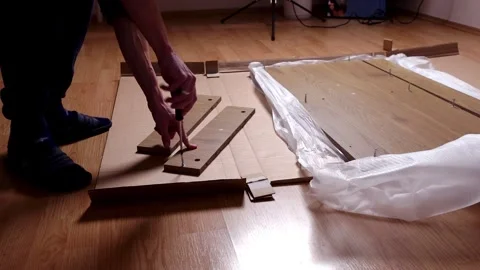 A young man twists a bolt with a screwdriver into a board. Furniture assembly Stock Footage 240954979