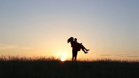 Young man twists on hands his woman in love on the rivers edge. Sunset light. Stock Footage 93563792