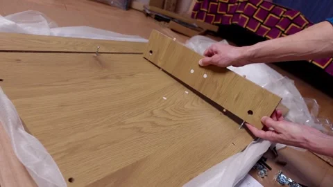 A young man twists a screw with a screwdriver into a board. Furniture assembly Stock Footage 240953976