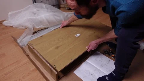 A young man twists a screw with a screwdriver into a board. Furniture assembly Stock Footage 240954036
