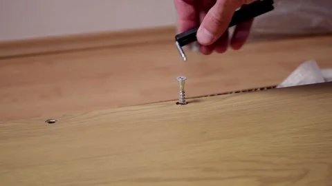 A young man twists a screw with a screwdriver into a board. Furniture assembly Stock Footage 240954076