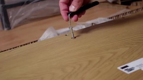 A young man twists a screw with a screwdriver into a board. Furniture assembly Stock Footage 240954077