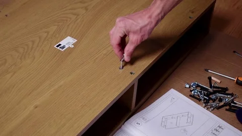 A young man twists a screw with a screwdriver into a board. Furniture assembly Stock Footage 240954096