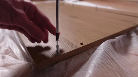 A young man twists a screw with a screwdriver into a board. Furniture assembly Stock Footage 240980845