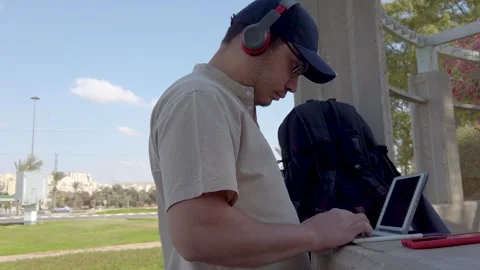 Young man types on a tablet keyboard in a park on a sunny day. Stock Footage 324927029