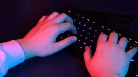A young man is typing on a computer keyboard. Hands close up. Blue and red light Stock Footage 125777412