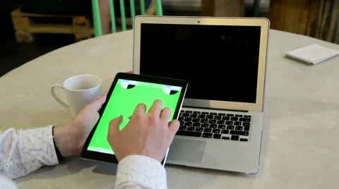 Young man typing on a laptop computer with a tablet with greenscreen Stockbeeldmateriaal 62802752