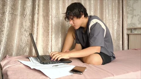 A young man is typing on a laptop keyboard, sitting on a bed in a room Stock Footage 311653862