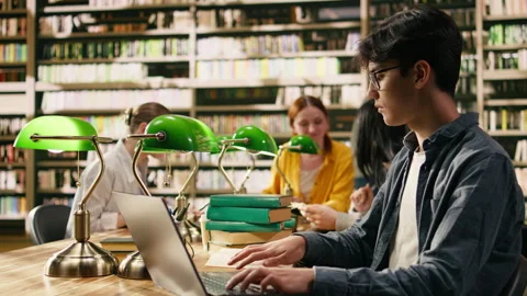 Young man typing on laptop in library study space and learning online Stock Footage 336358997