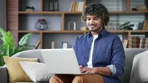Young man typing on laptop sitting on sofa in living room at home. Freelancer  Stock Footage 297867372
