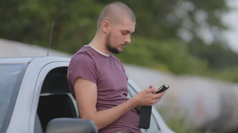 Young man typing a message on a smartphone in the street near the car Video stock 53280949