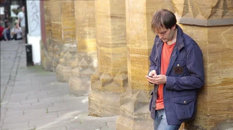 Young man typing a message with the smartphone standing on the sidewalk Video stock 56963885