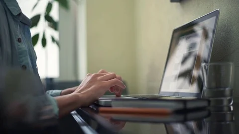 Young man typing message using laptop at home. Glass of water, notepad on desk Stock Footage 82926473