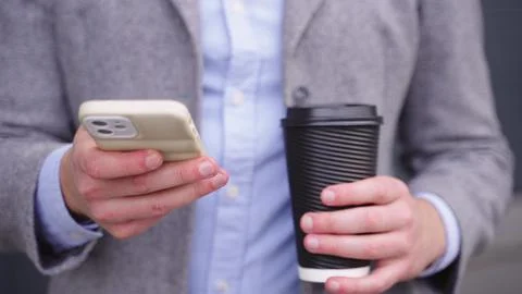 Young man typing on the phone while holding coffee. Slow motion Stock Photos