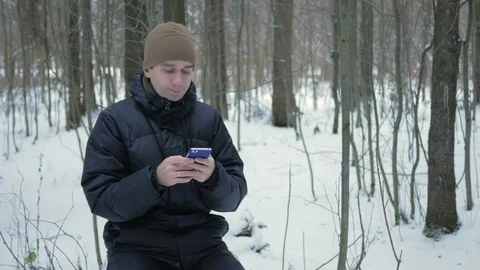 Young man typing a sms message on the phone in the winter snowy forest. He Stock Footage 71210275