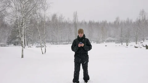 Young man typing a sms message on the phone in the winter snowy forest. Big Stock Footage 71217229