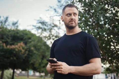 Young man typing text message on mobile phone outdoors in the park. Stock Photos