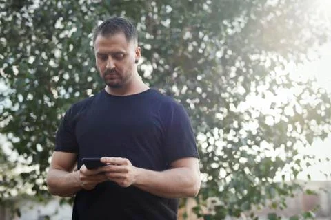 Young man typing text message on mobile phone outdoors in the park. Stock Photos
