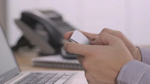 A young man typing with thumbs on a smartphone in office with laptop and phone Video stock 68447130