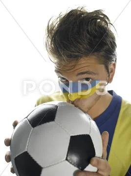 Young man with Ukrainian flag painted on face, kissing soccer ball, portrait Stock Photos