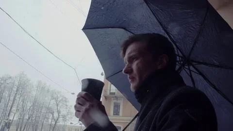 Young man with umbrella standing under snowfall drinking coffee from plastic cup Stock Footage 74894132