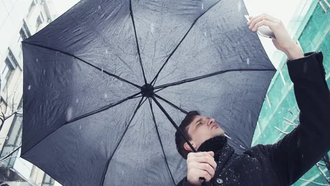 Young man with umbrella under snowfall making selfie photo using smartphone Stock Footage 74895816