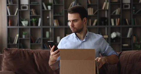 Young man unboxing parcel, checking order in mobile shopping app. Vidéo 161683934