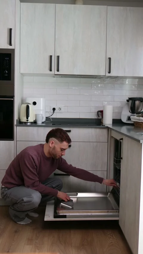 Young man unloading clean plates from dishwasher Stock Footage 333094600