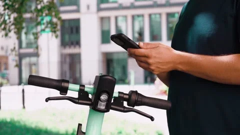 Young man unlocks an e-scooter with his mobile phone. Electric scooter new way Stock Footage 248841455