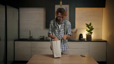 Young man unpacking clothes in paper bag at home.Guy opening parcel box standing Stock Footage 221619403