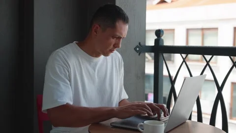 Young Man Use Laptop Computer On Terrace Drinking Coffe. Caucasian Man Typing Video stock 278618364