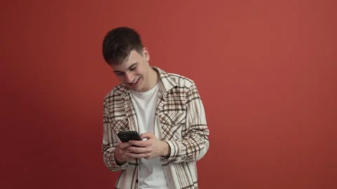 Young man use mobile phone stand in front red background studio shot Stock Footage 300789760