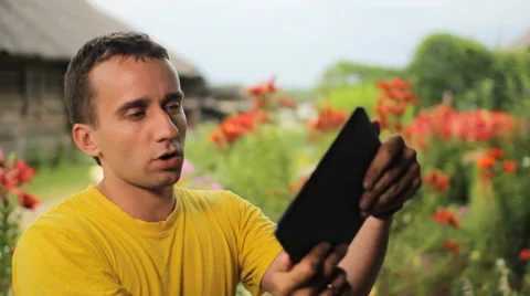 Young man use tablet for game near flowers in garden. White, red and purple Stock Footage 65093641