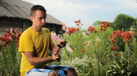 Young man use tablet for game near flowers in garden. White, red and purple Stock Footage 65093666