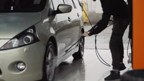 Young man uses a high pressure water jet to clean wheels on his car Stock Footage 144674634